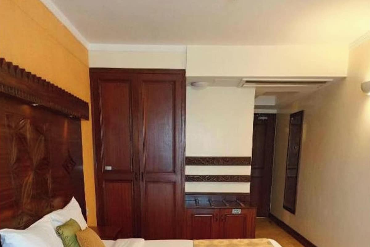 A hotel room with a bed, a wooden headboard, a wardrobe, and a bedside table.