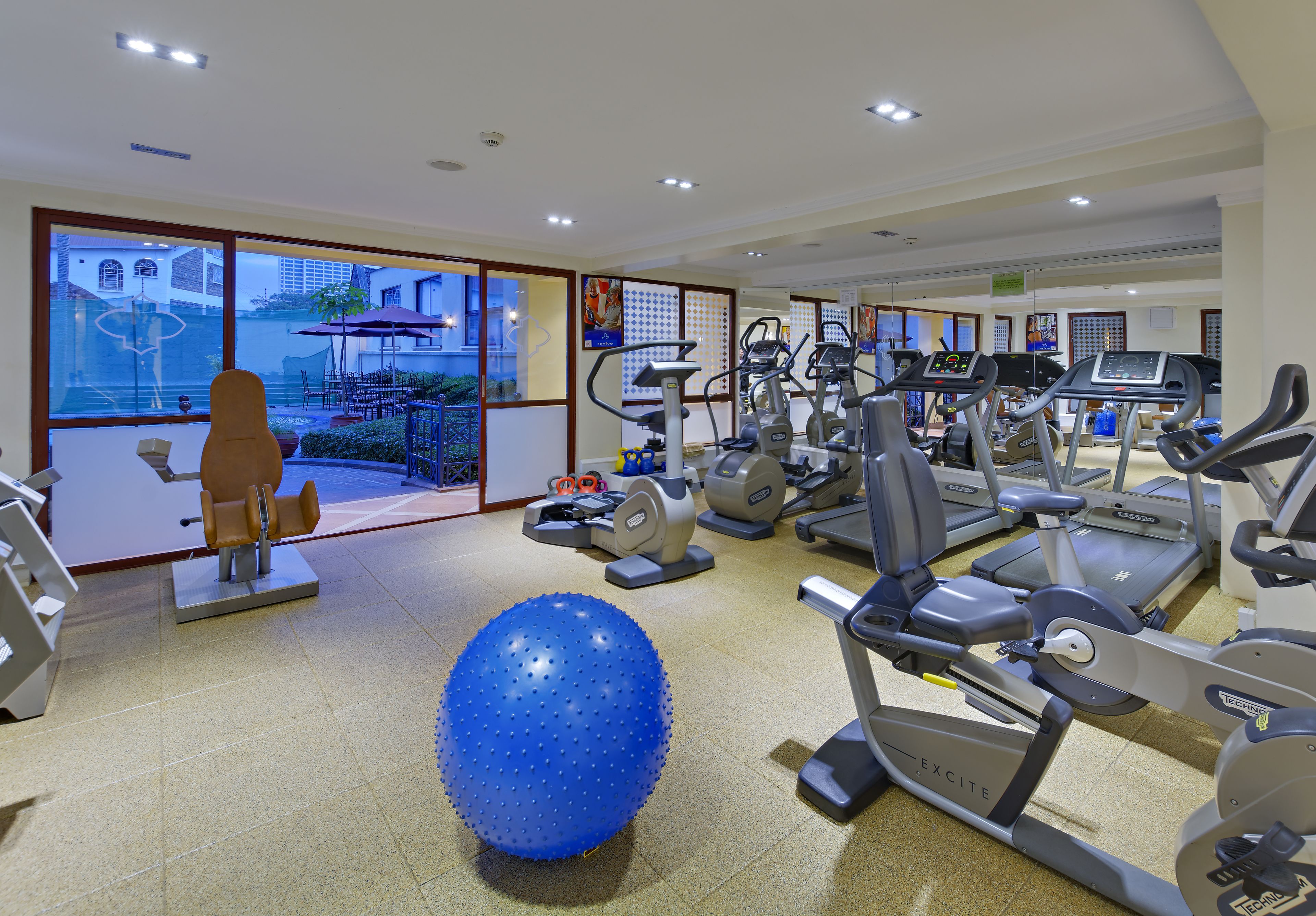 Ein Fitnessstudio mit unterschiedlichen Trainingsgeräten, einem großen blauen Übungsball und Blick durch große Fenster nach draußen.