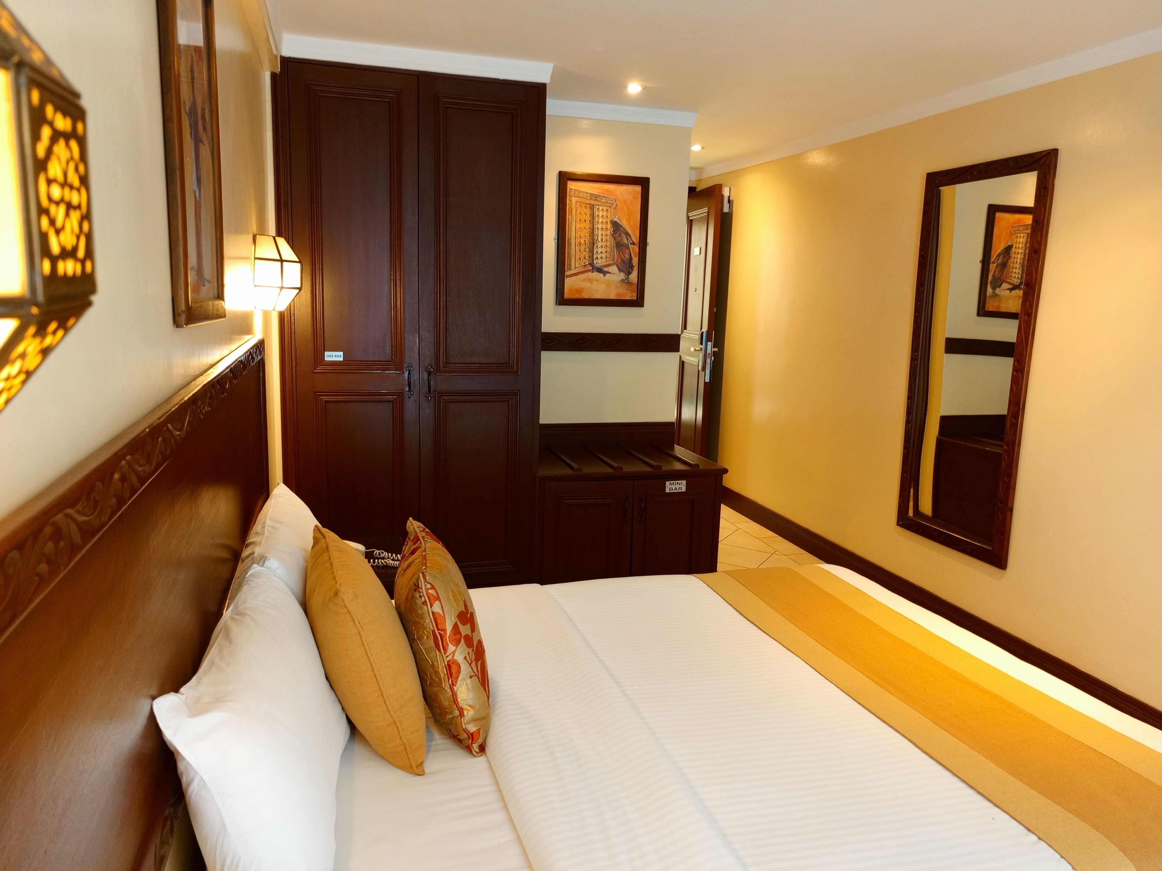 A hotel room with a large bed, a wardrobe, a vanity with a mirror, and a small table.