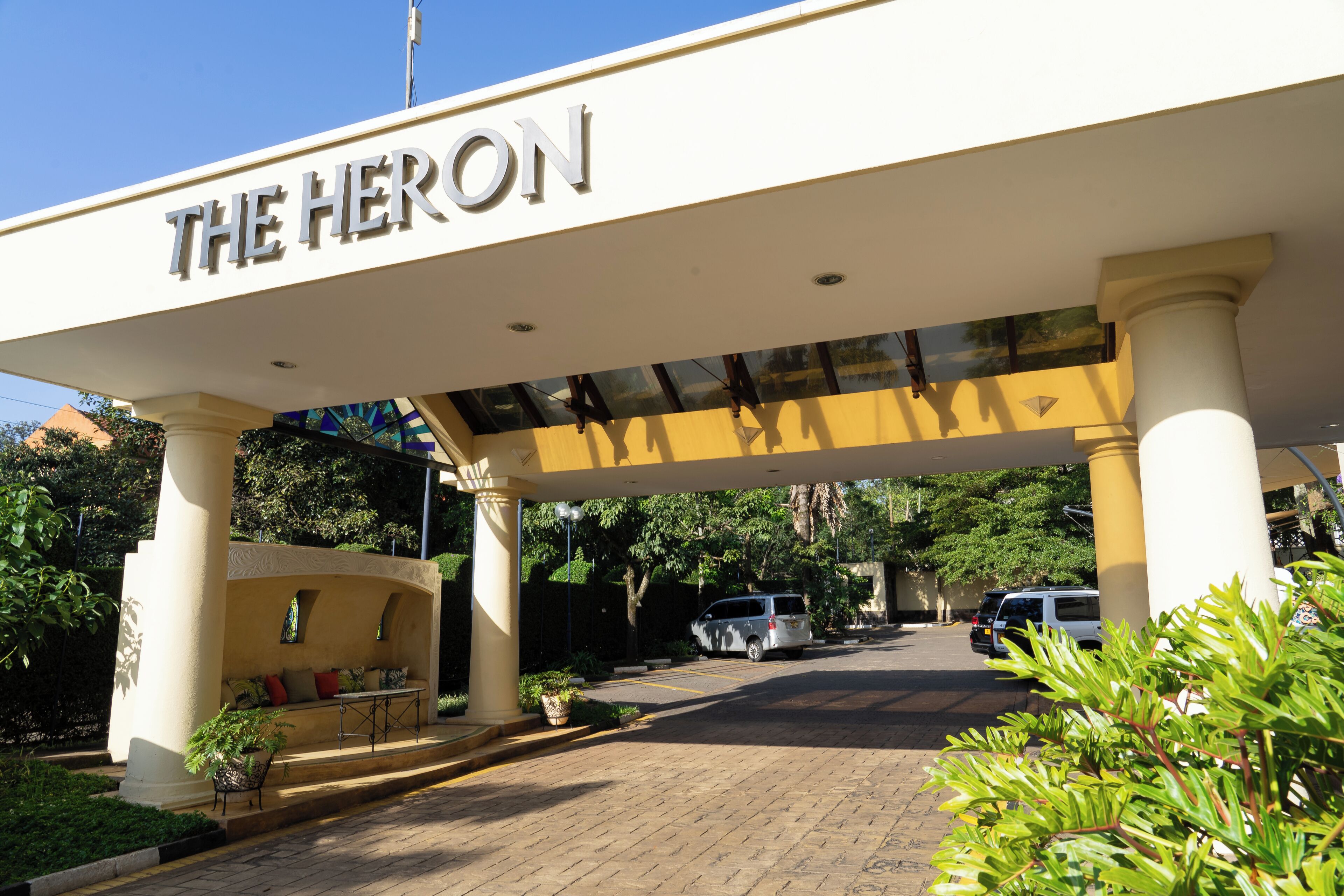 En hotellentrén med ett överhängande tak som bär inskriptionen ”THE HERON” och en asfalterad uppfart.