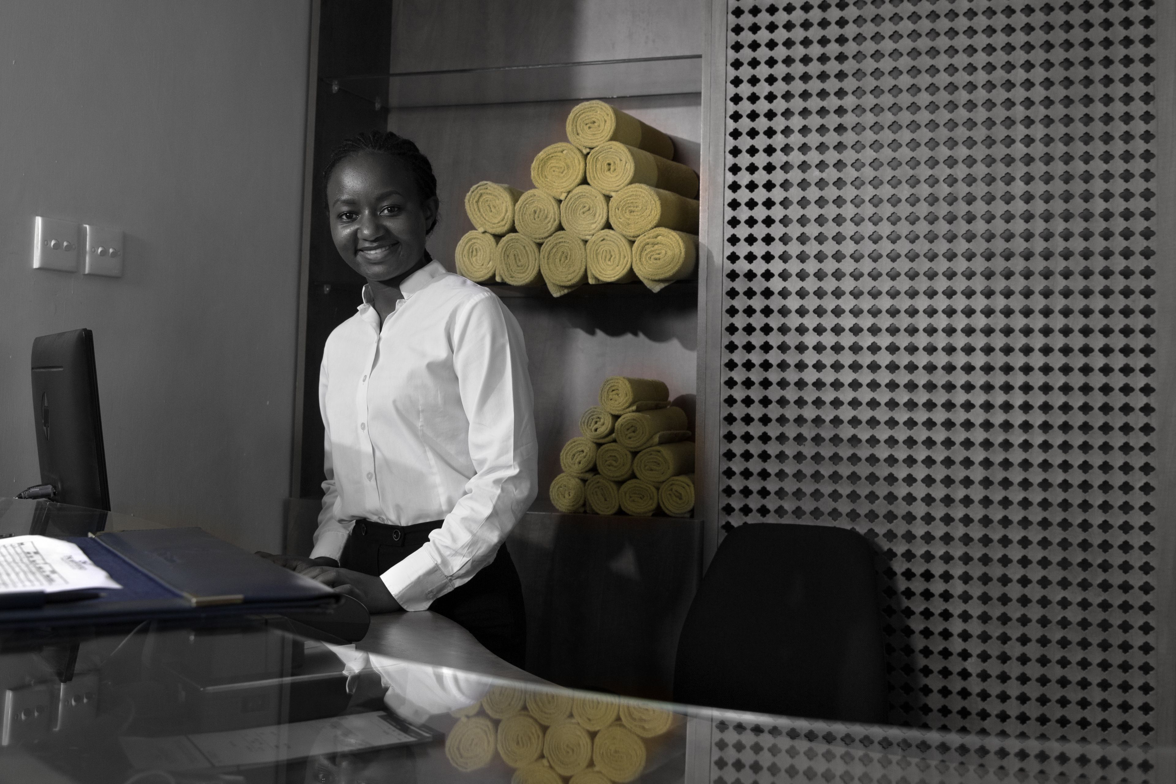 A person standing in an office with a desk, computer, and a wall with a patterned design.