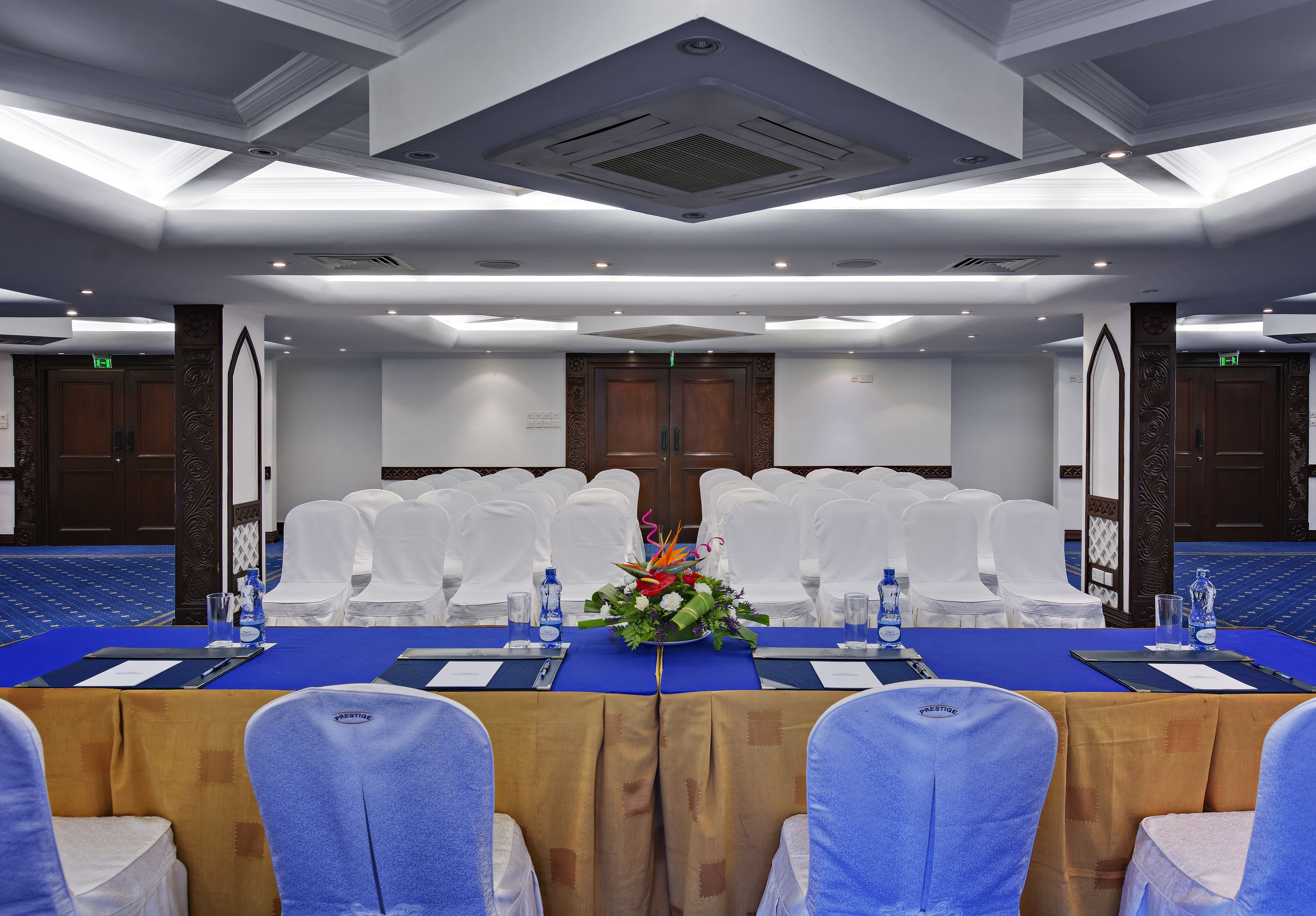 Una sala de conferencias con una larga mesa, sillas blancas y un centro de mesa floral.