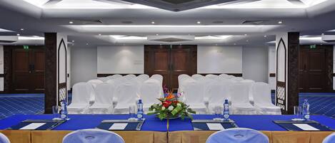 A conference room with a long table, white chairs, and a floral centerpiece.