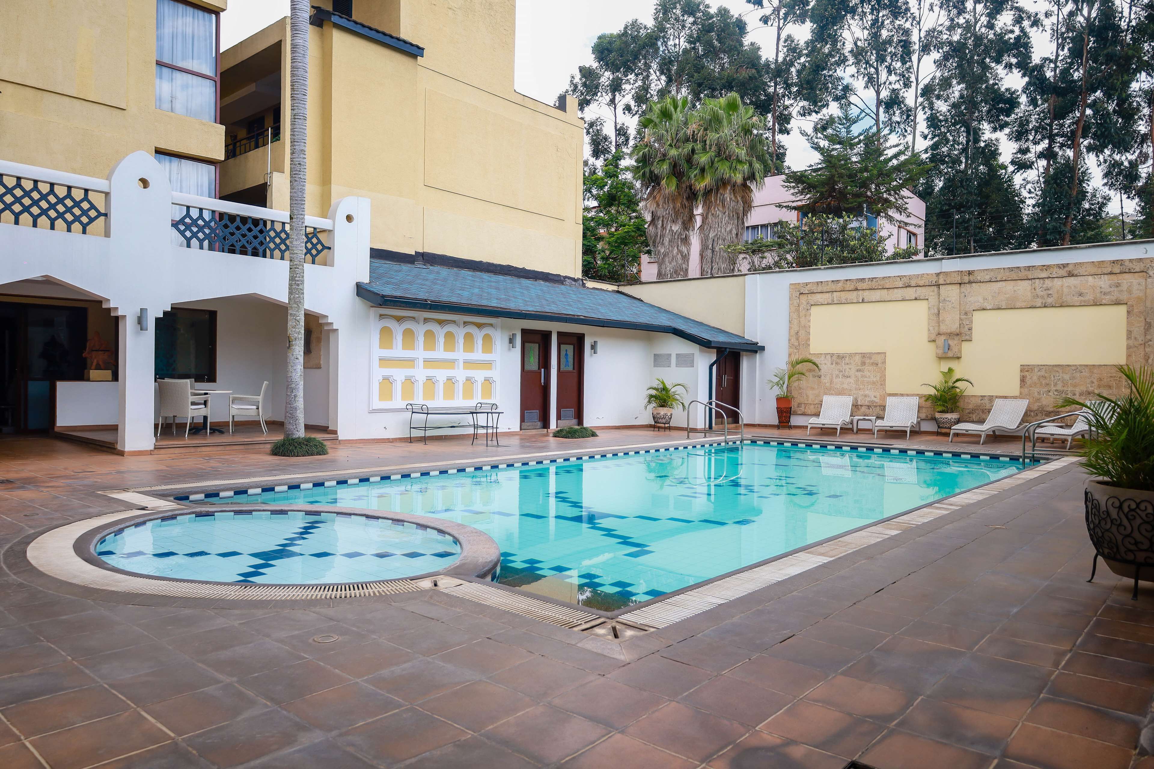 Una piscina con solárium de baldosas, rodeada por un edificio con balcones y mobiliario exterior.