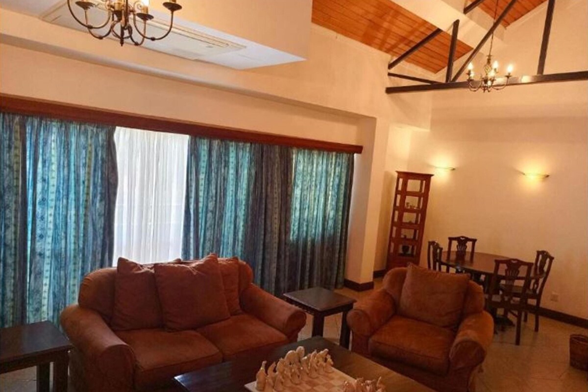 A living room with a sofa, armchair, and a small table with a decorative item. There is a dining area with a table and chairs.