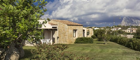 A stone house with a tiled roof, surrounded by a well-maintained lawn and trees.