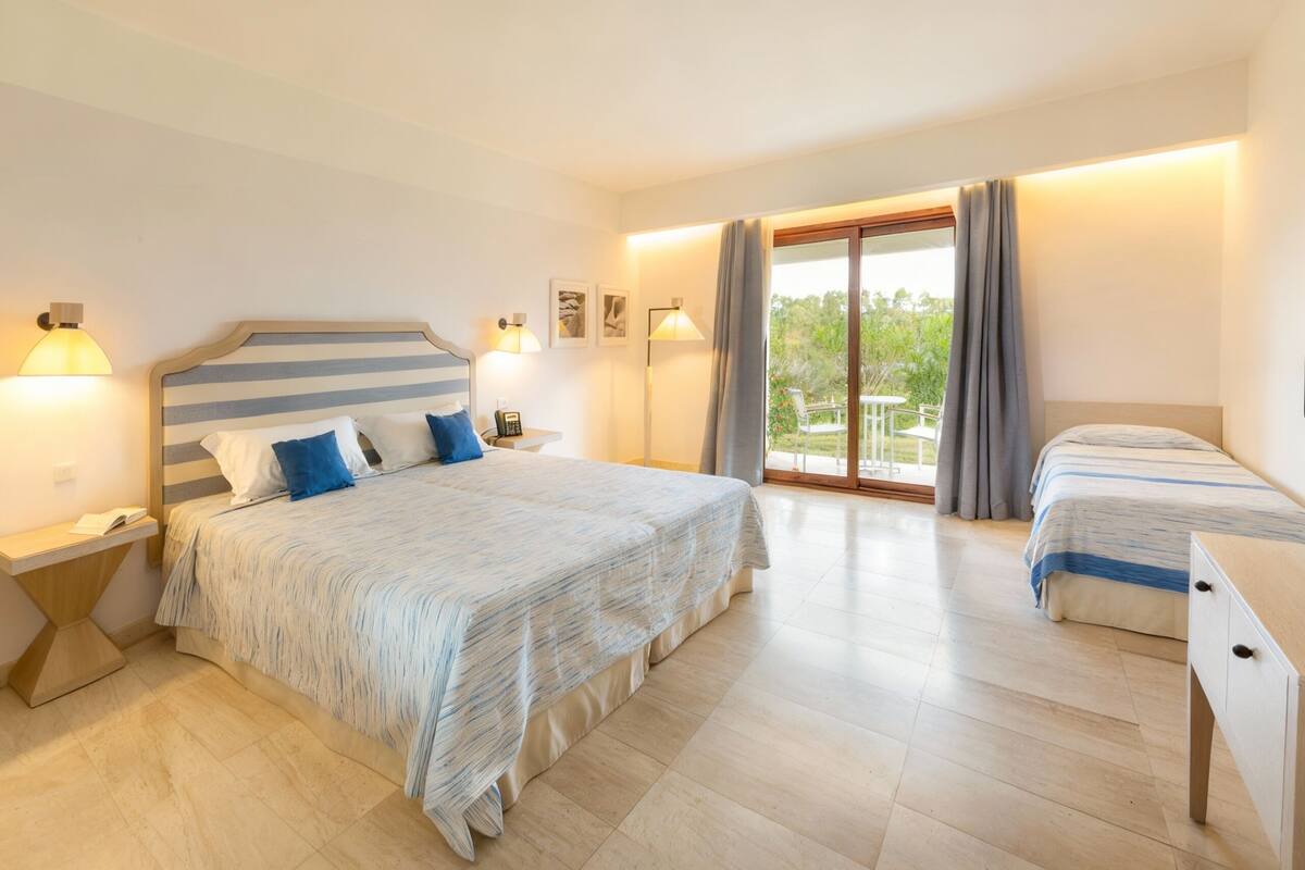 Een hotelkamer met een groot bed, een klein bed, een bureau en een balkon met gordijnen.
