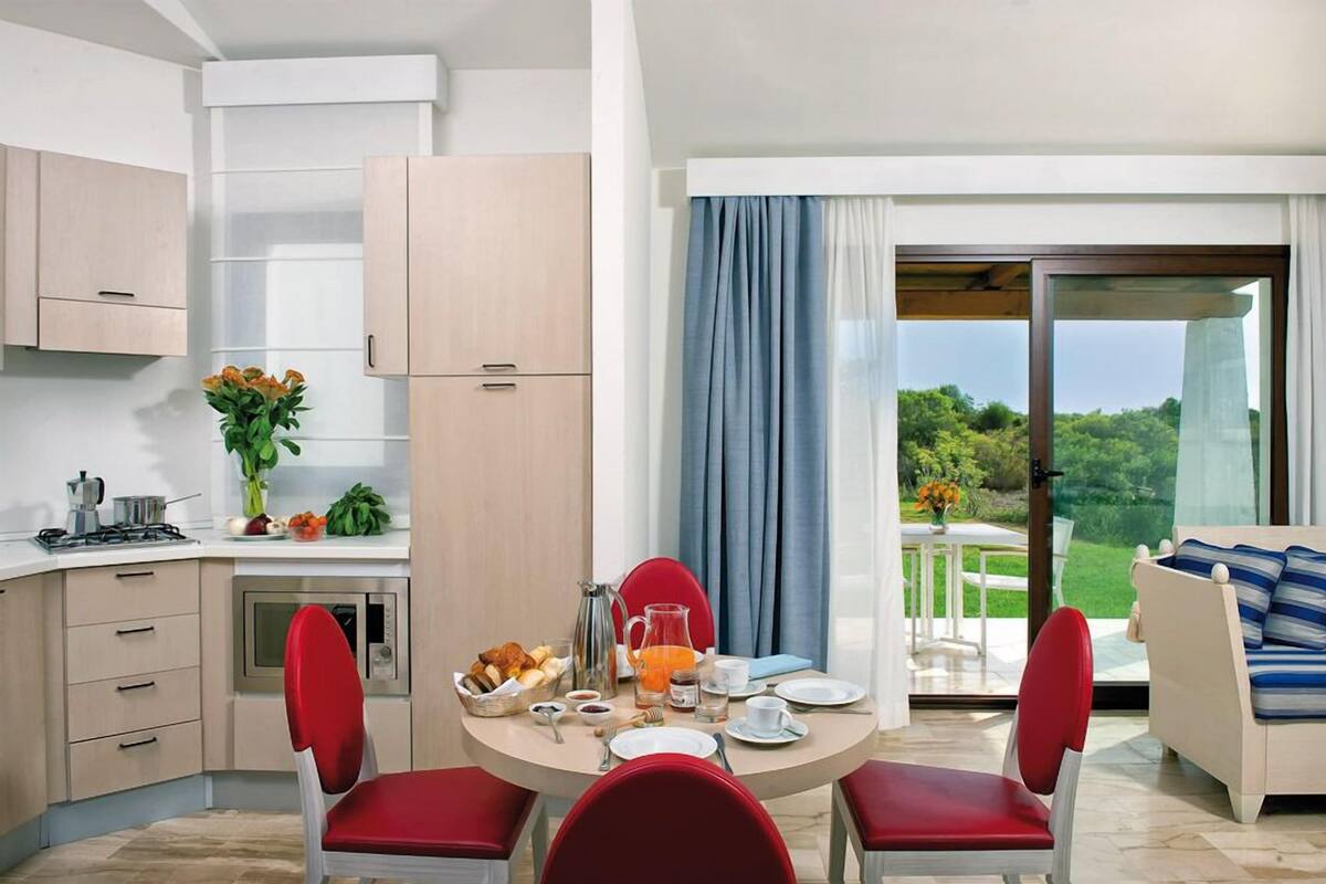 Een moderne keuken met een eethoek, een rode stoel, een ontbijttafel en uitzicht op groen via het raam.