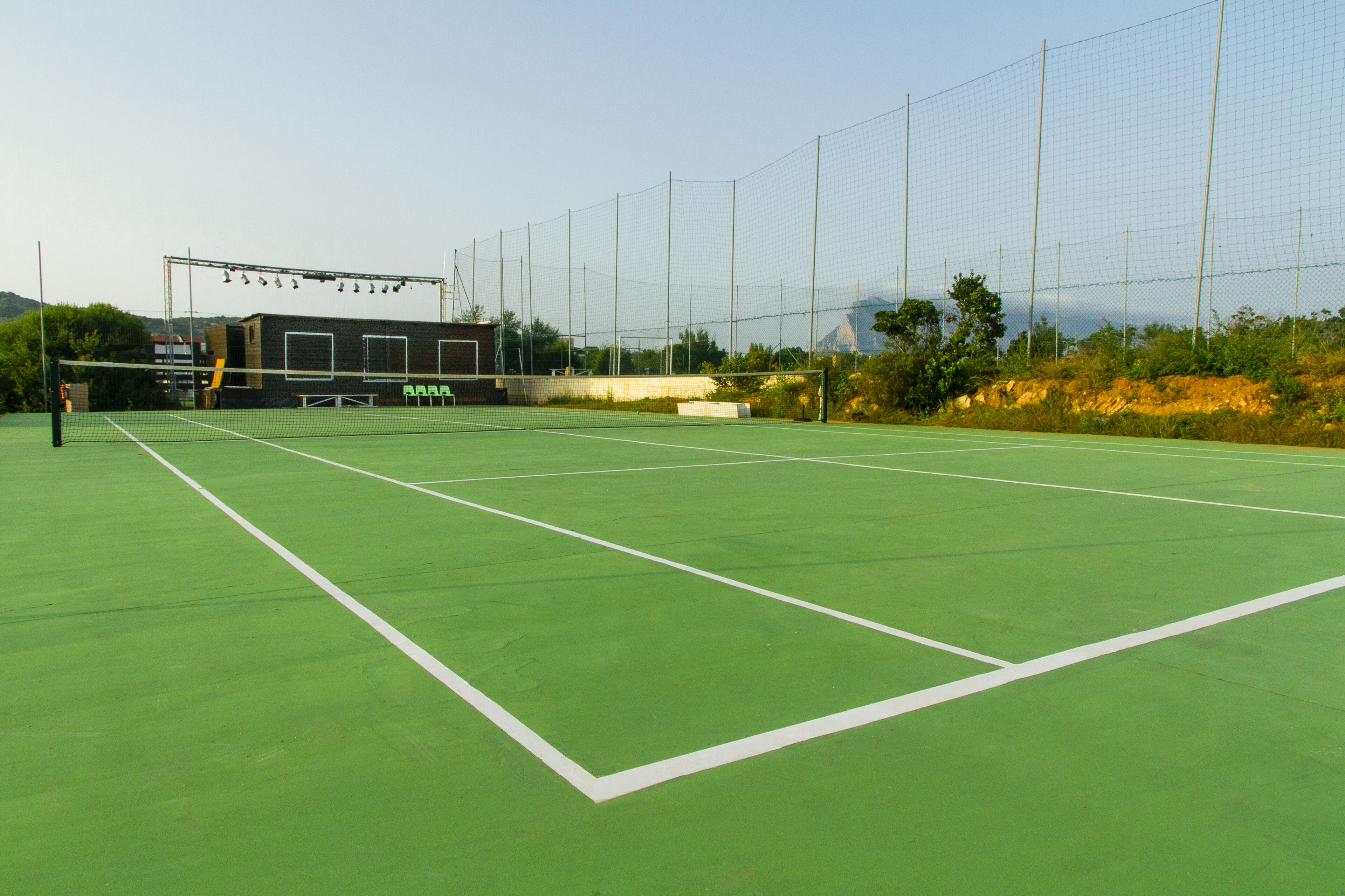 An outdoor tennis court with a net, seating area, and a backdrop of trees and hills.