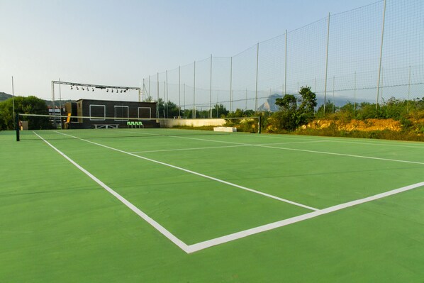 Una cancha de tenis al aire libre con red, zona de estar y un fondo de árboles y colinas.