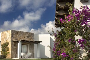 Un edificio moderno con fachada de piedra, un área de estar cubierta al aire libre y vibrantes flores moradas.
