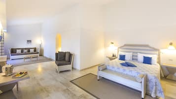 Una habitación de hotel con una cama, un sofá, una mesita con una bandeja de fruta y una mesita de noche con una lámpara.