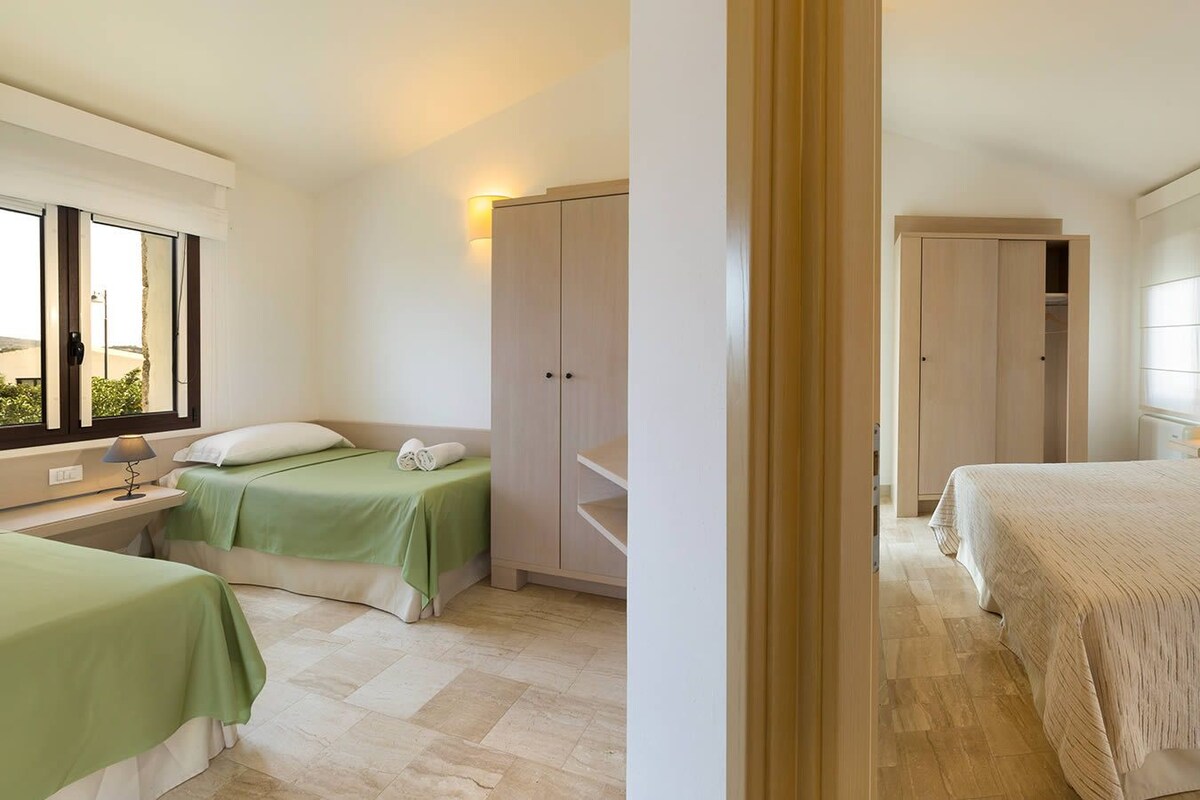 A hotel room with a bed, a desk with a lamp, a wardrobe, and a window with curtains.
