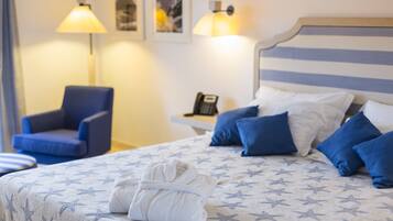 Una cama bien hecha con una colcha de estampado de estrellas, una bata doblada sobre la cama, un sillón azul y una mesita de noche con una lámpara y un teléfono.