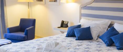 Een net opgemaakt bed met een sprei met stermotief, een opgevouwen badjas op het bed, een blauwe fauteuil en een nachtkastje met een lamp en een telefoon.