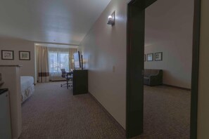 A hotel room with a bed, desk, chair, and a large window with curtains. - Comfort Inn & Suites San Bernardino (Colton)