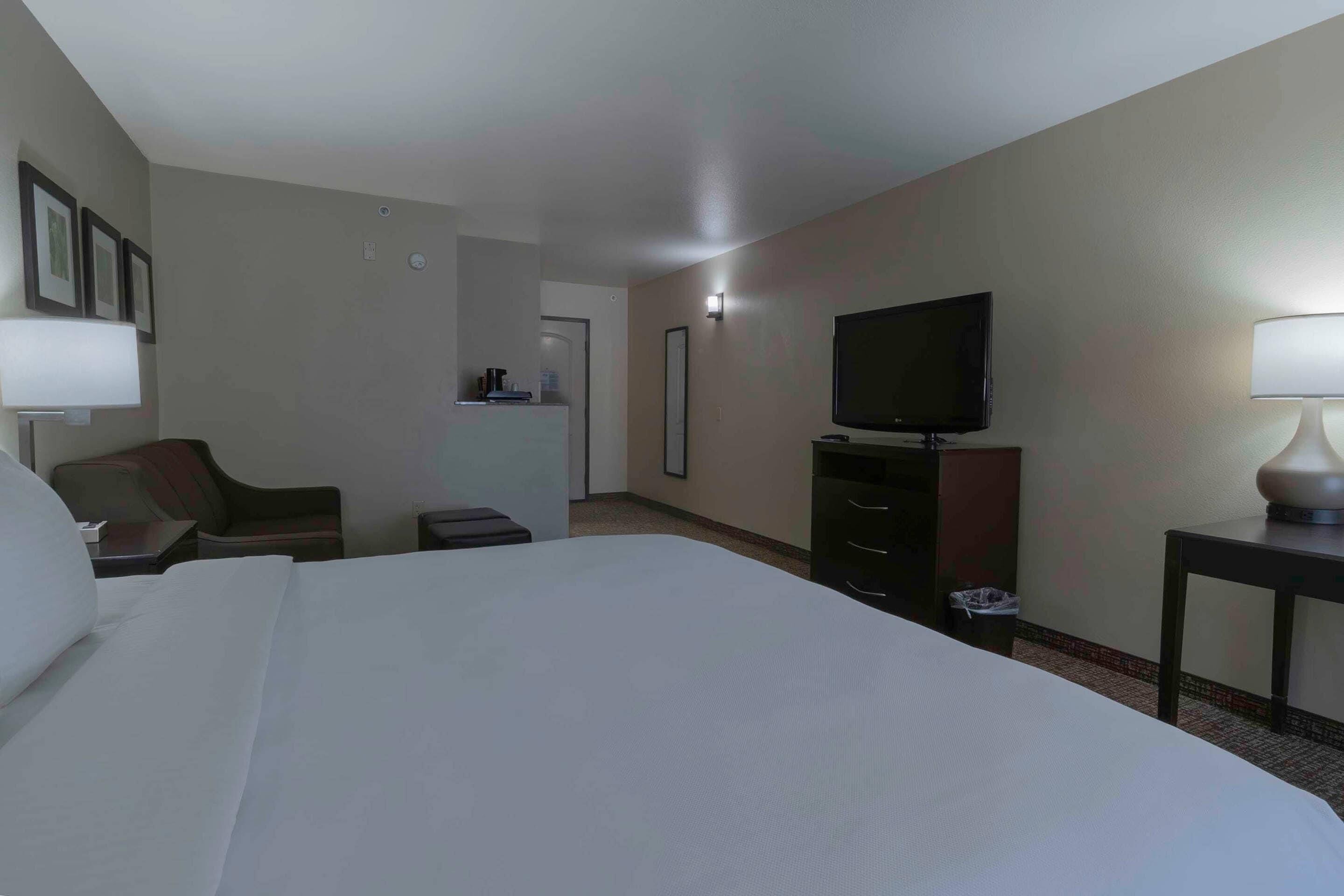 A hotel room with a bed, a television, a desk with a lamp, a chair, and a small table.