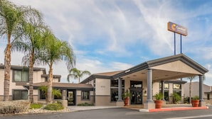 A hotel entrance with a covered area, palm trees, and a sign indicating it's a Comfort Inn & Suites. - Comfort Inn & Suites San Bernardino (Colton)