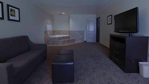 A room with a sofa, ottoman, TV, and a bathroom with a bathtub and shower. - Comfort Inn & Suites San Bernardino (Colton)