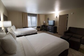 A hotel room with two beds, a television, a desk, and a sofa.