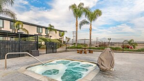 A hot tub in a courtyard with palm trees, a fence, and a building in the background. - Comfort Inn & Suites San Bernardino (Colton)