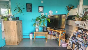 A room with a teal wall, a wooden cabinet, a TV, a bookshelf, and various plants. - Tiki Village (Vernon)
