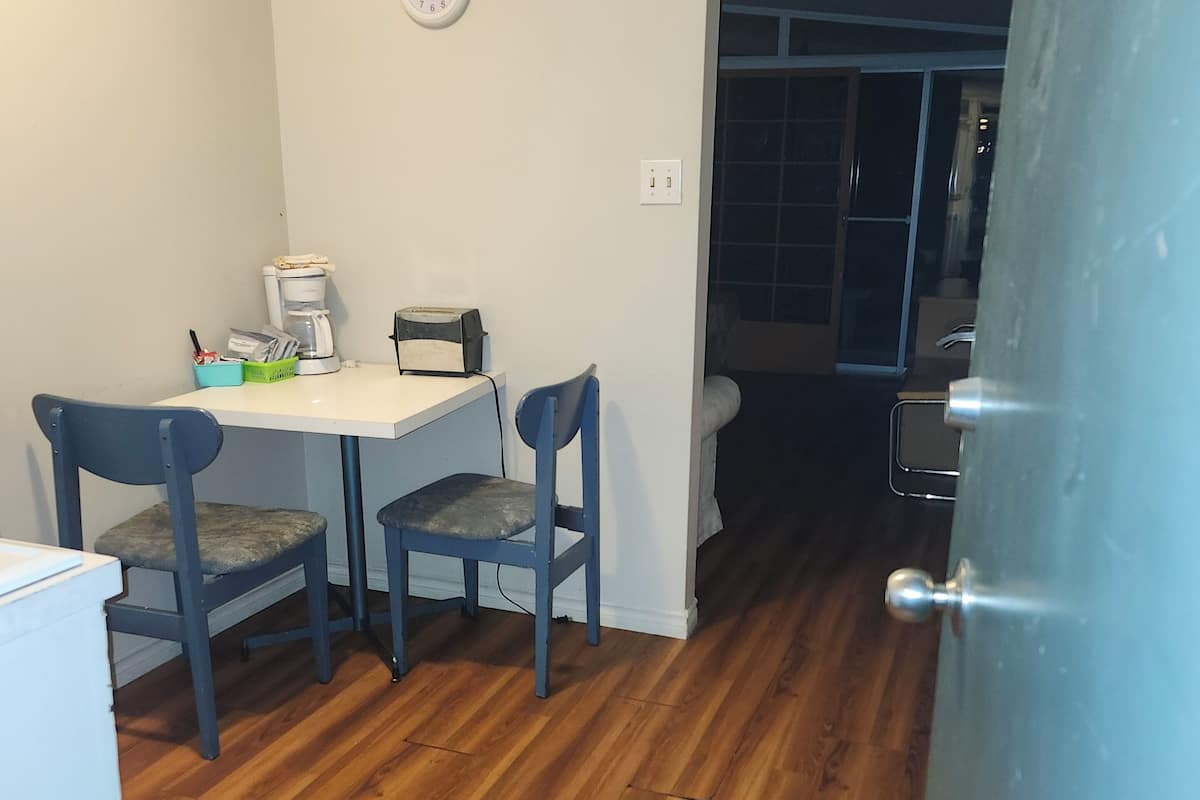 A compact room with a white table and two chairs, a clock on the wall, and a door leading to another room.