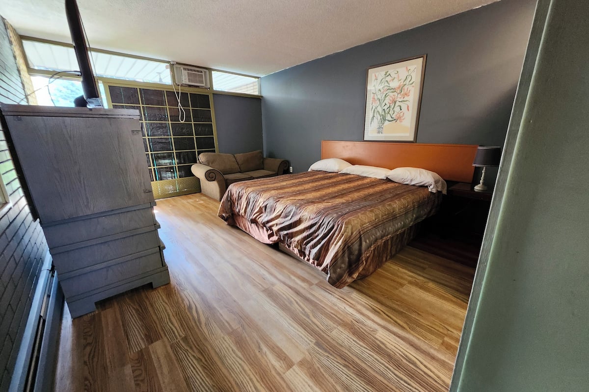A bedroom with a bed, a sofa, a dresser, and a window with blinds.