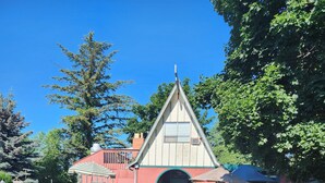 A quaint, triangular-roofed building with a circular entrance, surrounded by a decorative fence and lush greenery. - Tiki Village (Vernon)