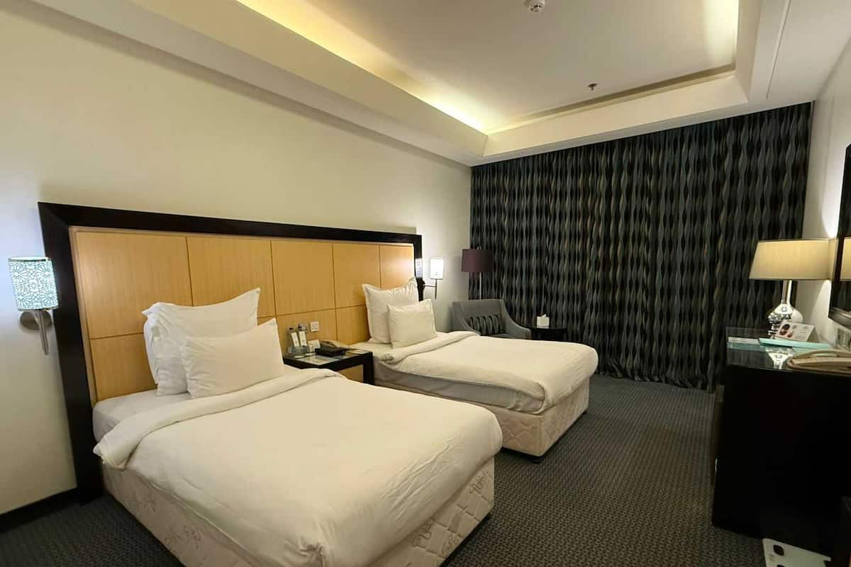 Habitació d'hotel amb dos llits, un escriptori, una cadira, una làmpada i una cortina.