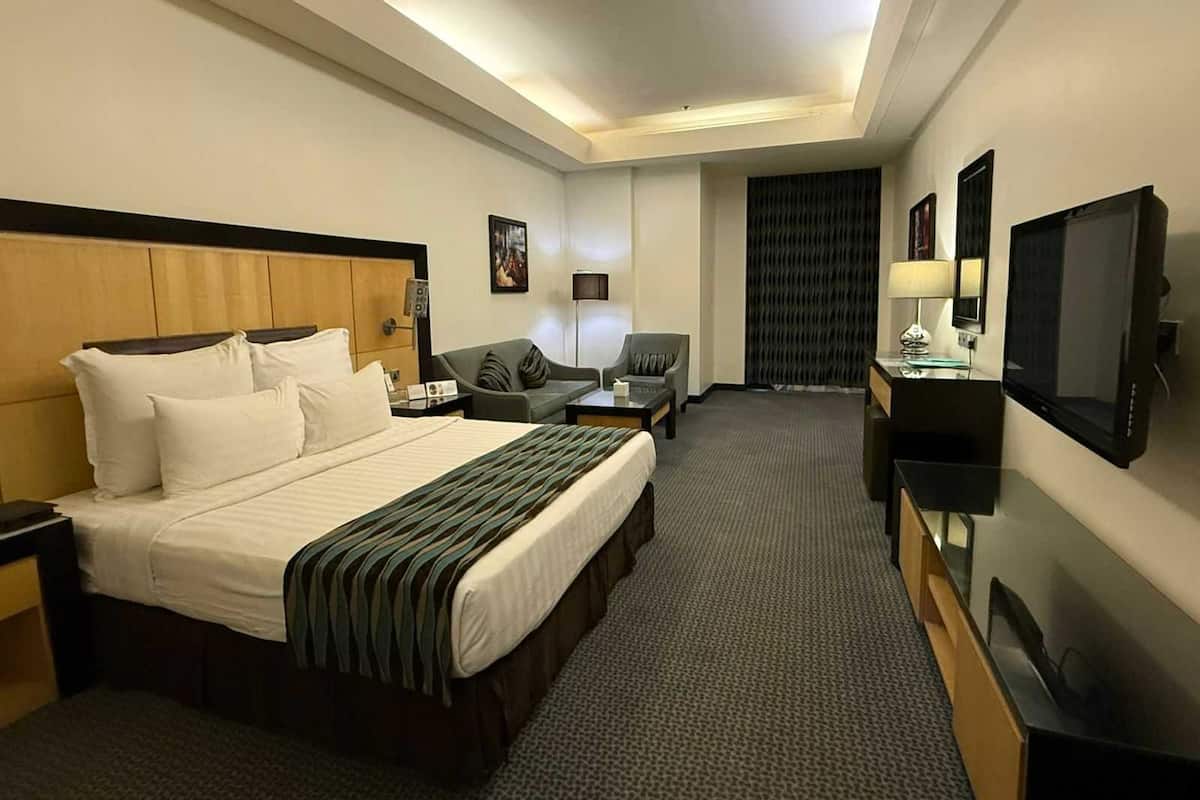 Una habitació d'hotel amb un llit gran, un escriptori amb un televisor, una cadira i un sofà.