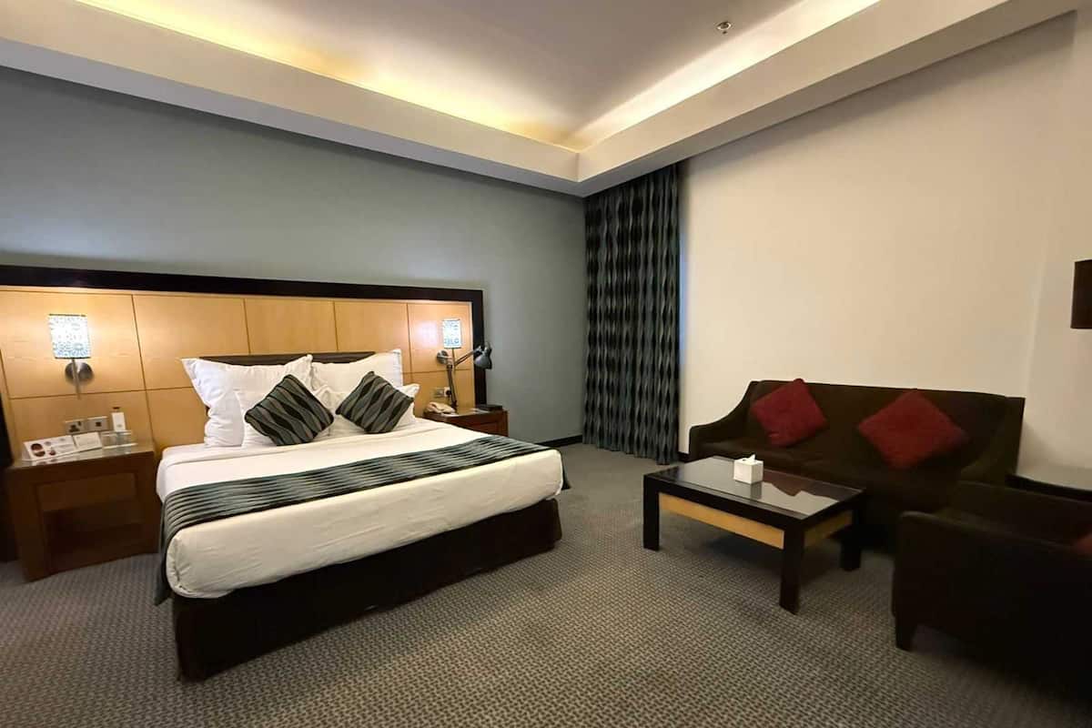 Habitació d'hotel amb un llit gran, una taula de nit, un sofà, una taula de cafè i una cortina.