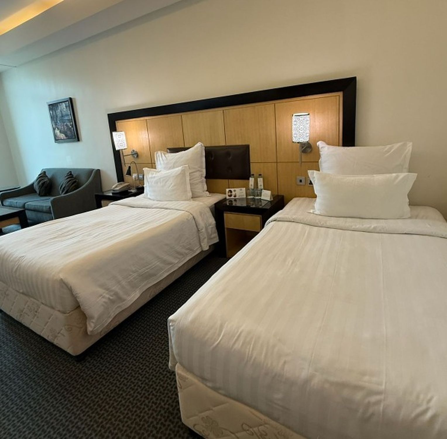 A hotel room with two beds, a desk, a chair, and a sofa.