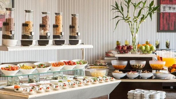 Montaje de bufé con diversas opciones de comida y bebidas, como frutas, ensaladas y aperitivos.