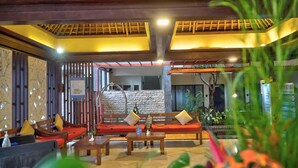 A lobby with a wooden ceiling, a stone wall, and a seating area with red cushions and wooden furniture. - Best Western Resort Kuta (Kuta)
