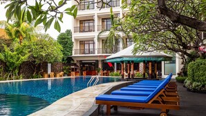 A swimming pool with lounge chairs, a wooden deck, and a building with balconies in the background. - Best Western Resort Kuta (Kuta)