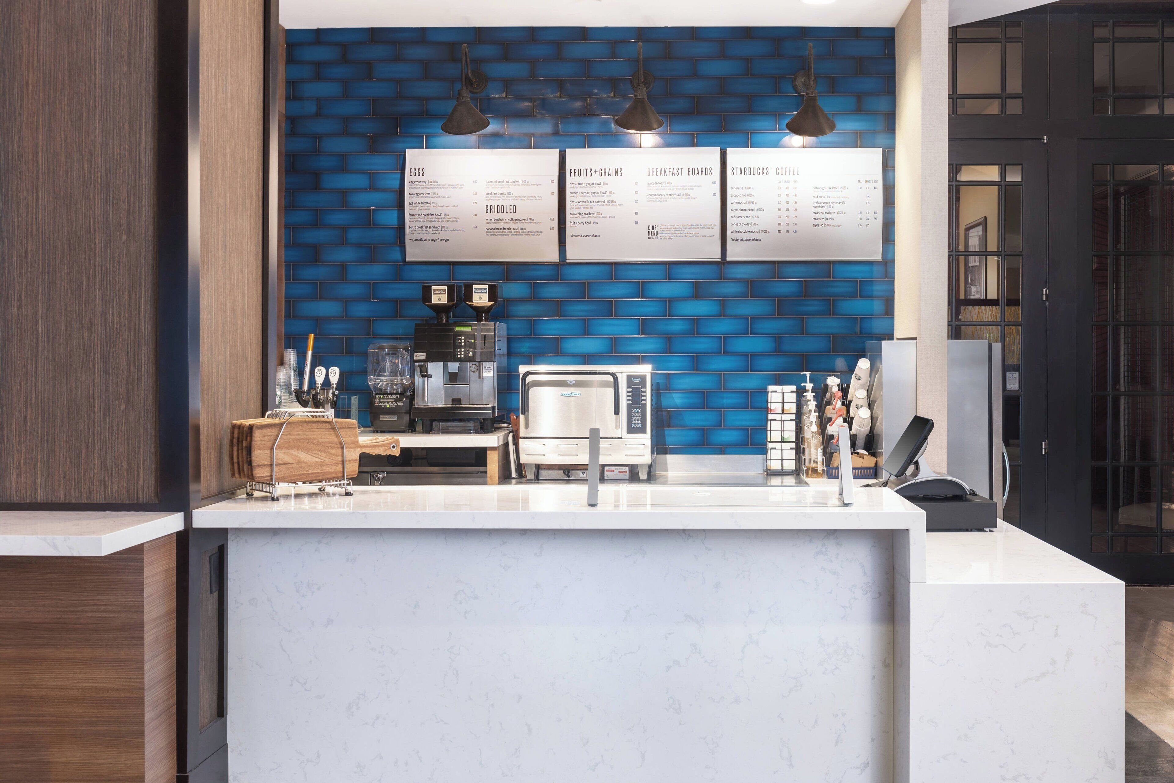 A modern kitchen with a marble countertop, a coffee machine, and a menu board.