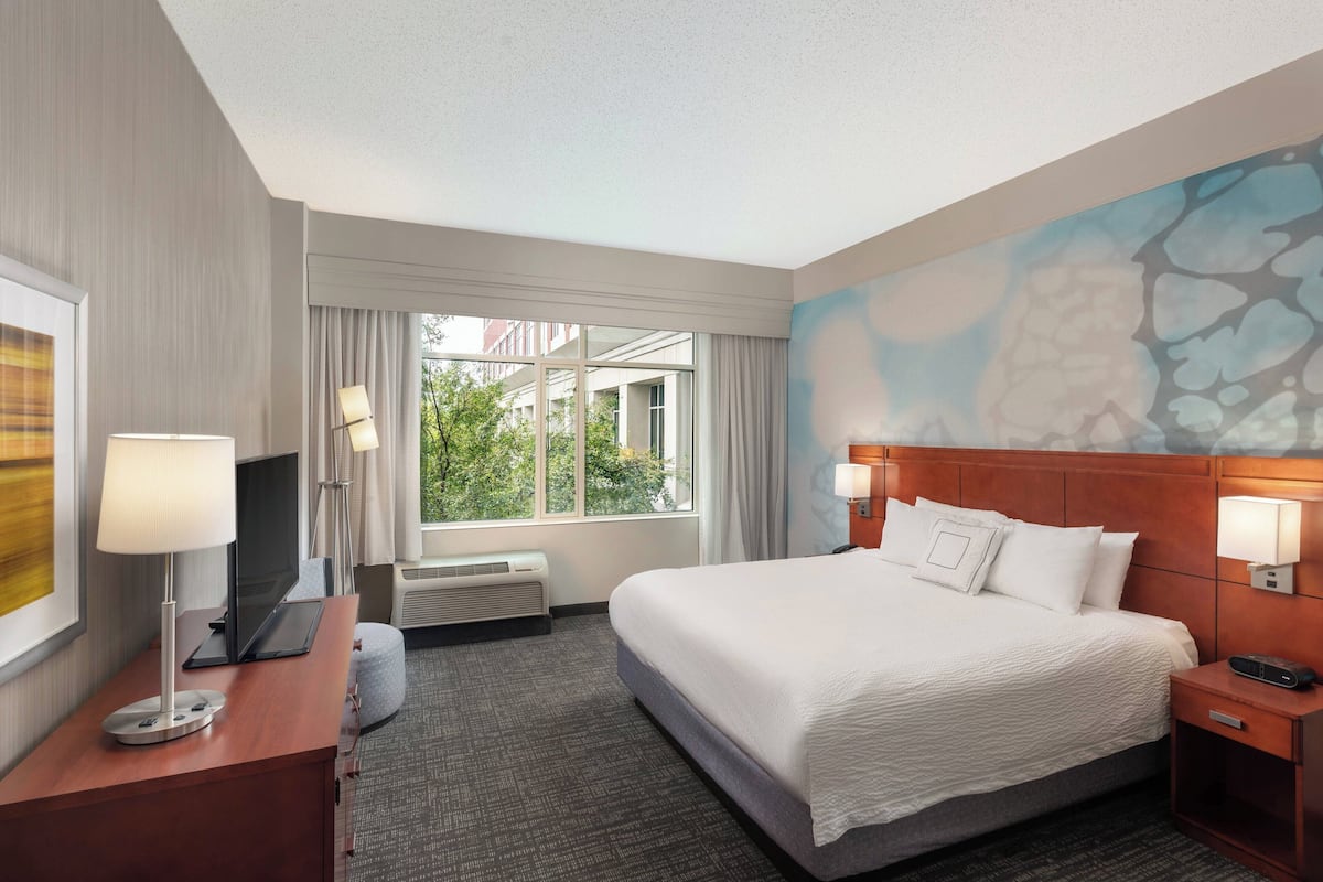A hotel room with a large bed, a desk with a lamp, a TV, and a window with curtains.