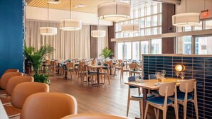 A spacious dining area with multiple tables and chairs, large windows, and hanging pendant lights. - Courtyard by Marriott Greenville Downtown (Greenville)