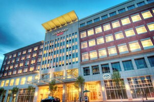 Un hotel Courtyard Marriott con diseño moderno, que presenta una entrada destacada con puertas de vidrio y un corredor cubierto.