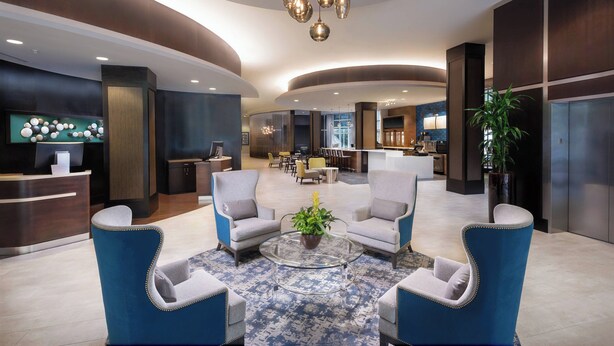 A modern lobby with a reception desk, seating area, and a kitchen in the background. - Courtyard by Marriott Greenville Downtown (Greenville)
