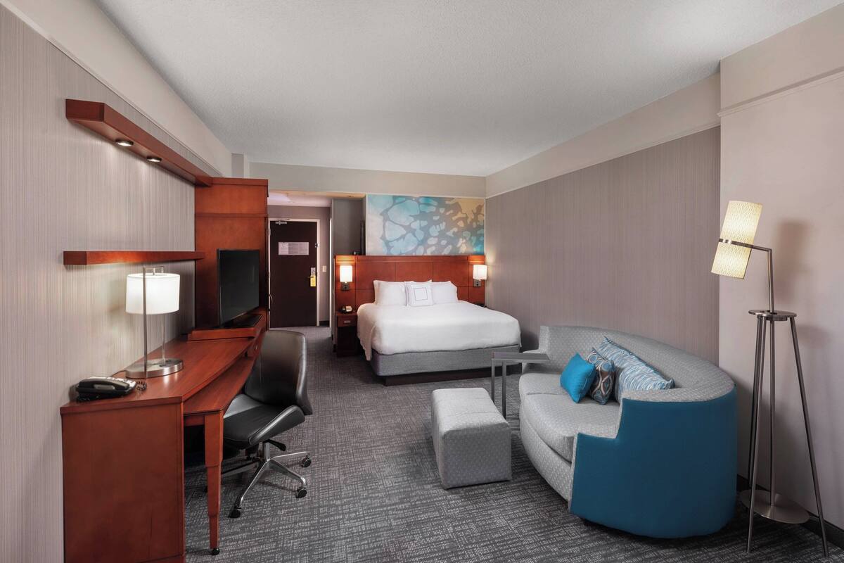 A hotel room with a bed, a desk, a sofa, and a standing lamp.