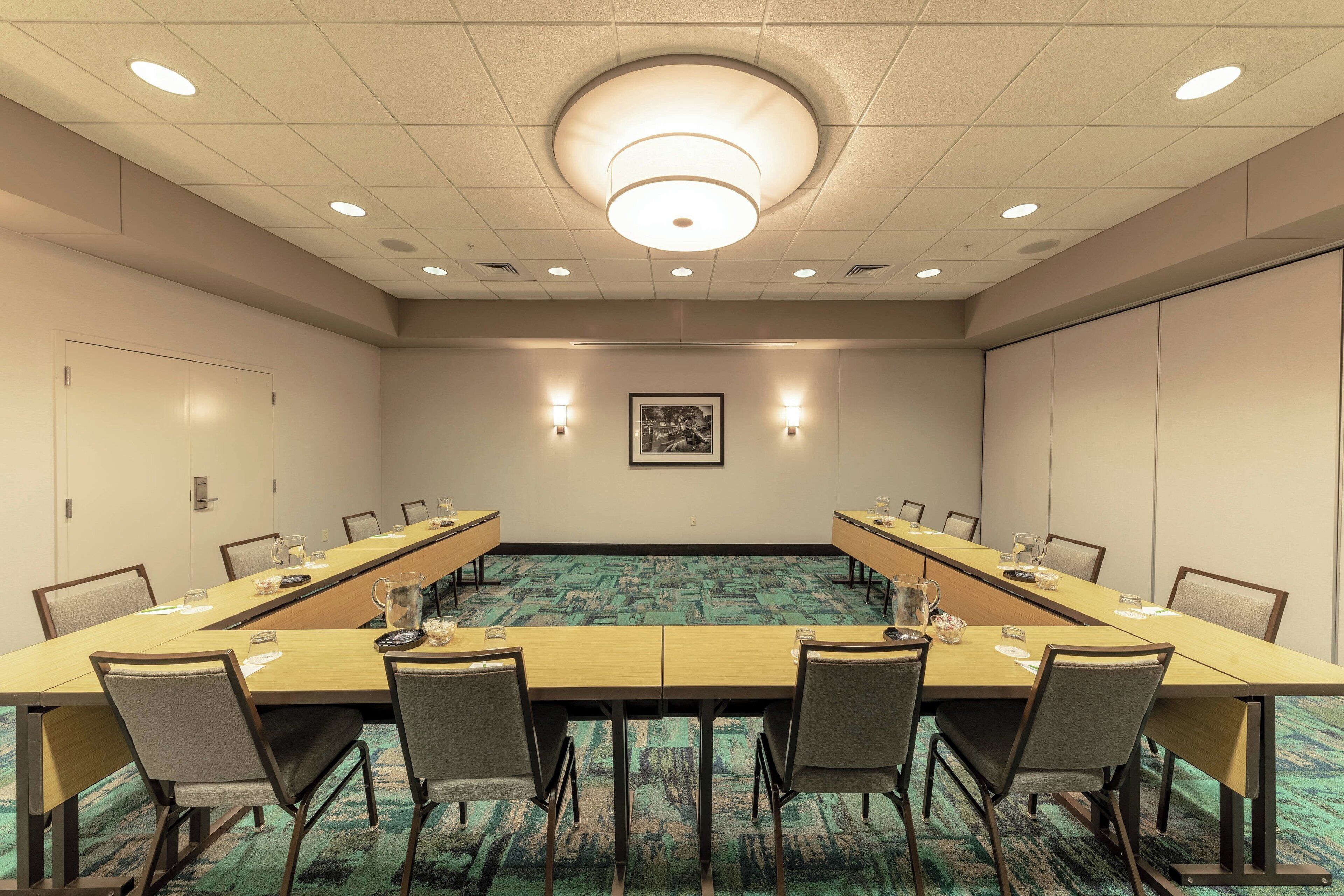 A conference room with a long table, chairs, a carpeted floor, and a ceiling light fixture.