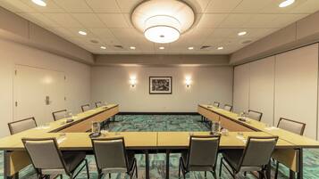 A conference room with a long table, chairs, a carpeted floor, and a ceiling light fixture.