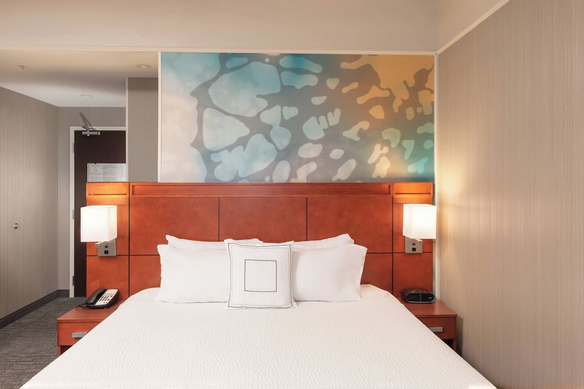 A hotel room with a large bed, two bedside lamps, a telephone, and a wall-mounted artwork.