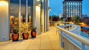 A hotel exterior with large windows, outdoor seating, and potted plants. - Courtyard by Marriott Greenville Downtown (Greenville)