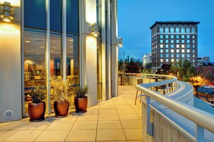 Exterior de un hotel con amplios ventanales, mobiliario exterior y plantas en macetas.