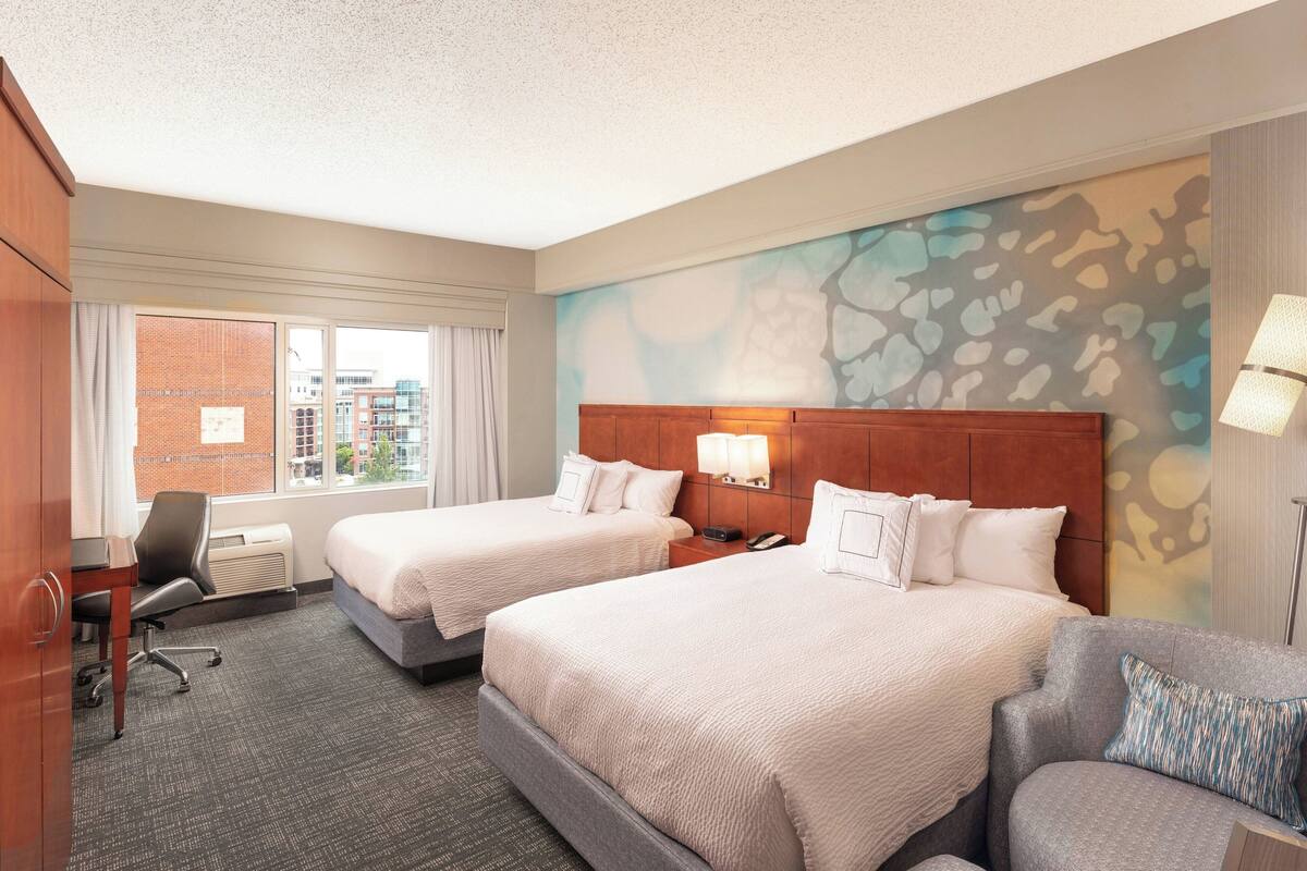 A hotel room with two beds, a desk, a chair, and a couch.