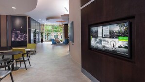 A modern hotel lobby with a large digital display, seating areas, and a view of the outdoors. - Courtyard by Marriott Greenville Downtown (Greenville)