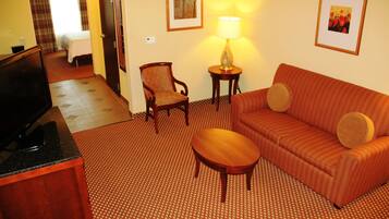 Habitación de hotel con sofá, sillón, mesa, televisor, lámpara y obras de arte en las paredes.
